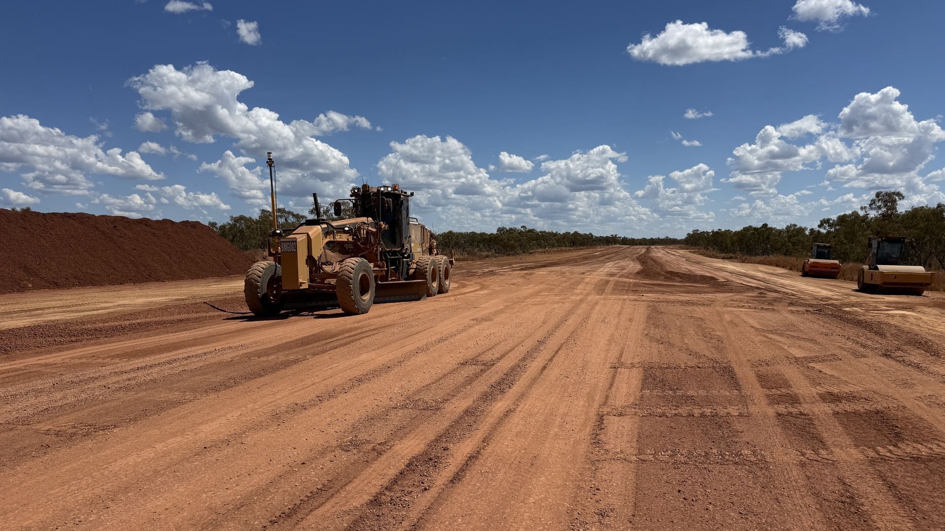 Banksia grader trimming a red-dirt road with rollers behind